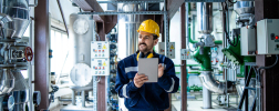 Flow rate is calculated by a man wearing a yellow safety helmet and carrying a tablet in a plant.