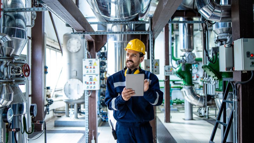 Flow rate is calculated by a man wearing a yellow safety helmet and carrying a tablet in a plant.