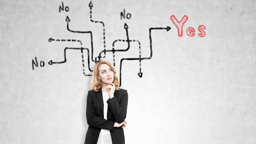 Portrait of a redhead woman standing near a concrete wall with arrows leading to yes, no or no answer. Concept of difficulties of making a choice I